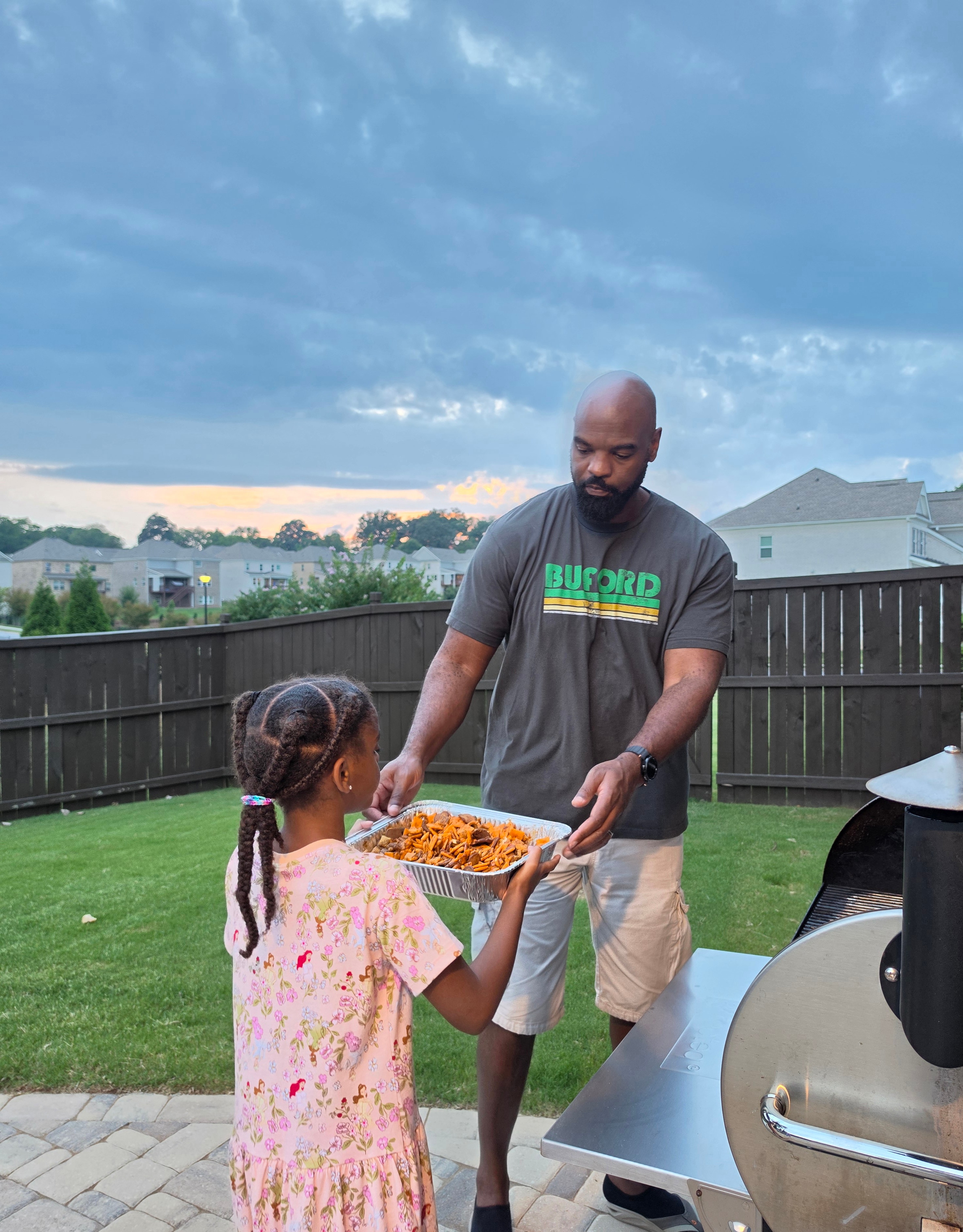 Chonsey and Luna carrying a tray of snack mix together beside the smoker in Buford, Georgia